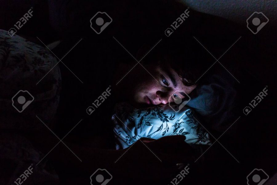 A teenager looking on his phone at night before he goes to bed. (Photo Courtesy of 123RF)