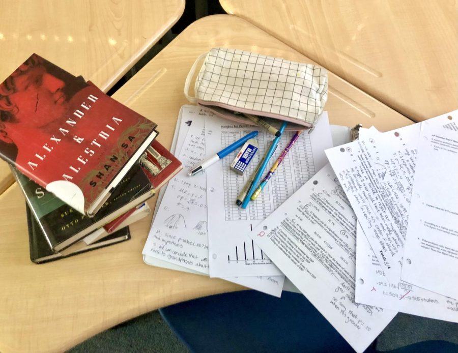 An array of books, homework, and school supplies scattered on a desk.
