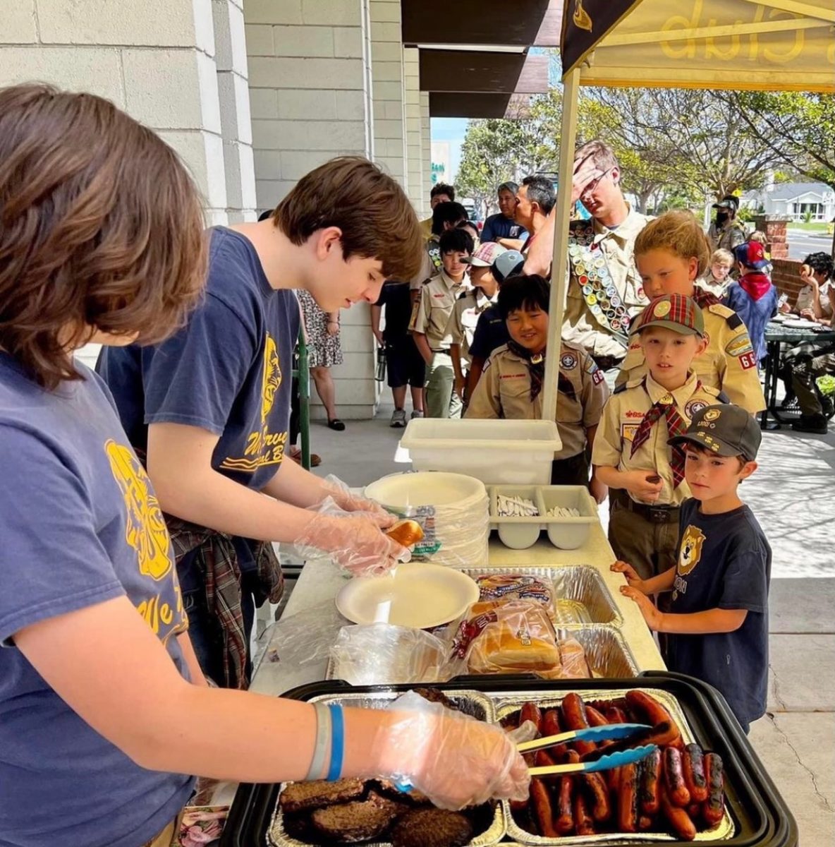 Leos club members cook and serve hot dogs to Cub Scouts at a volunteering event.