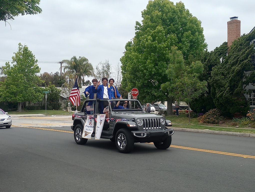 Senior boys wave from their Jeep parade vehicle, decorated with banners and American flags.