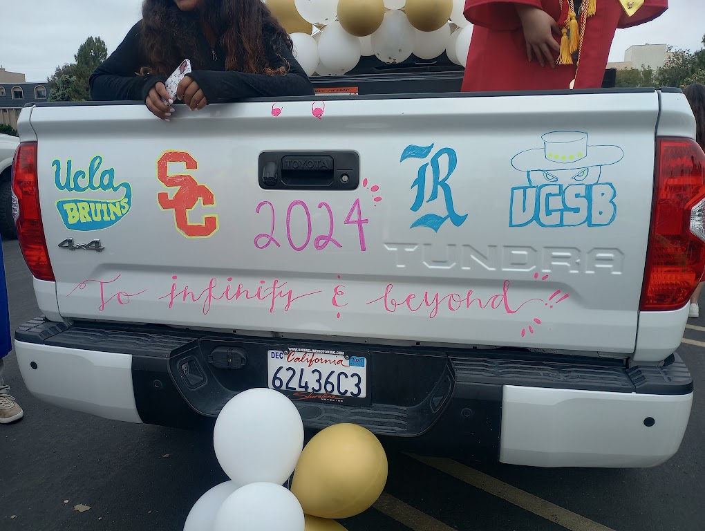 A parade vehicle is decorated with college logos, with the phrase To infinity & beyond below.