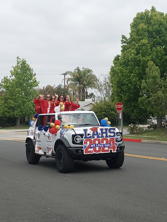 Senior girls wave from the back of their white Jeep parade vehicle, decorated with a custom graduation sign and balloons.
