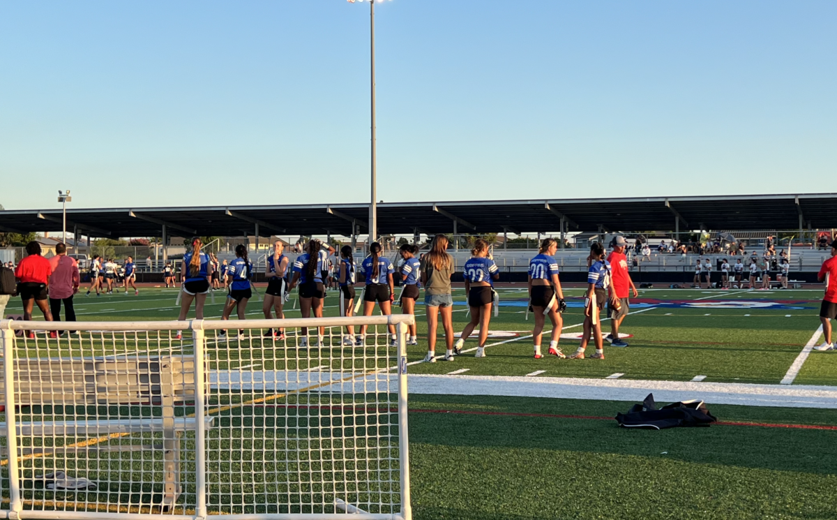 The girls flag football players watch their teammates play against their opponents during the second half of the game. 