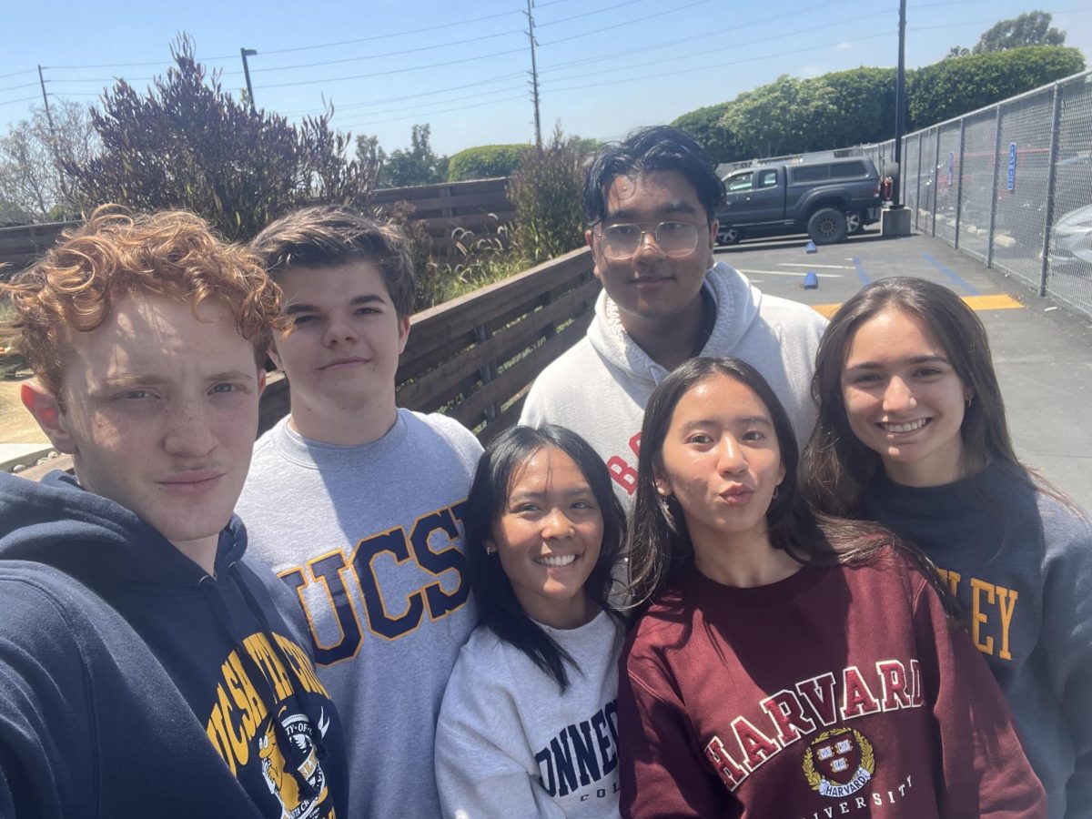 Jack Fredlund, Noah Hedgie Revell, Roshan Rajalingam, Sydney Concepcion, Kaitlyn Mady and Mira Zacheis in a group selfie, all with sweaters representative of their respective schools. 