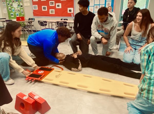 At the start of class, Coach Bowe demonstrated the supine roll. He picked several students to help with the demonstration and had the rest of the class stand in a circle to watch. The "patient," junior Kenneth Mao, laid on the floor in the middle of the circle. As Coach Bowe controlled Mao's head and shoulders to prevent a spinal injury, the students helped him roll Mao on his side. One student then pushed the board against Mao's side, and the group rolled him onto the board. The group made a few minor adjustments to Mao's positioning before adding velcro blocks to hold his head in place. "Last year it was pretty fun, and I have a potential career in this field, so I thought Advanced Sports Medicine was a good pathway to go through," Mao said. "It's very interactive and fun, and you meet a lot of people. I didn't know any of these people coming into this class. Now I'm like best friends with all of them."