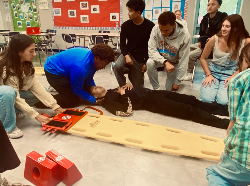 At the start of class, Coach Bowe demonstrated the supine roll. He picked several students to help with the demonstration and had the rest of the class stand in a circle to watch. The "patient," junior Kenneth Mao, laid on the floor in the middle of the circle. As Coach Bowe controlled Mao's head and shoulders to prevent a spinal injury, the students helped him roll Mao on his side. One student then pushed the board against Mao's side, and the group rolled him onto the board. The group made a few minor adjustments to Mao's positioning before adding velcro blocks to hold his head in place. "Last year it was pretty fun, and I have a potential career in this field, so I thought Advanced Sports Medicine was a good pathway to go through," Mao said. "It's very interactive and fun, and you meet a lot of people. I didn't know any of these people coming into this class. Now I'm like best friends with all of them."