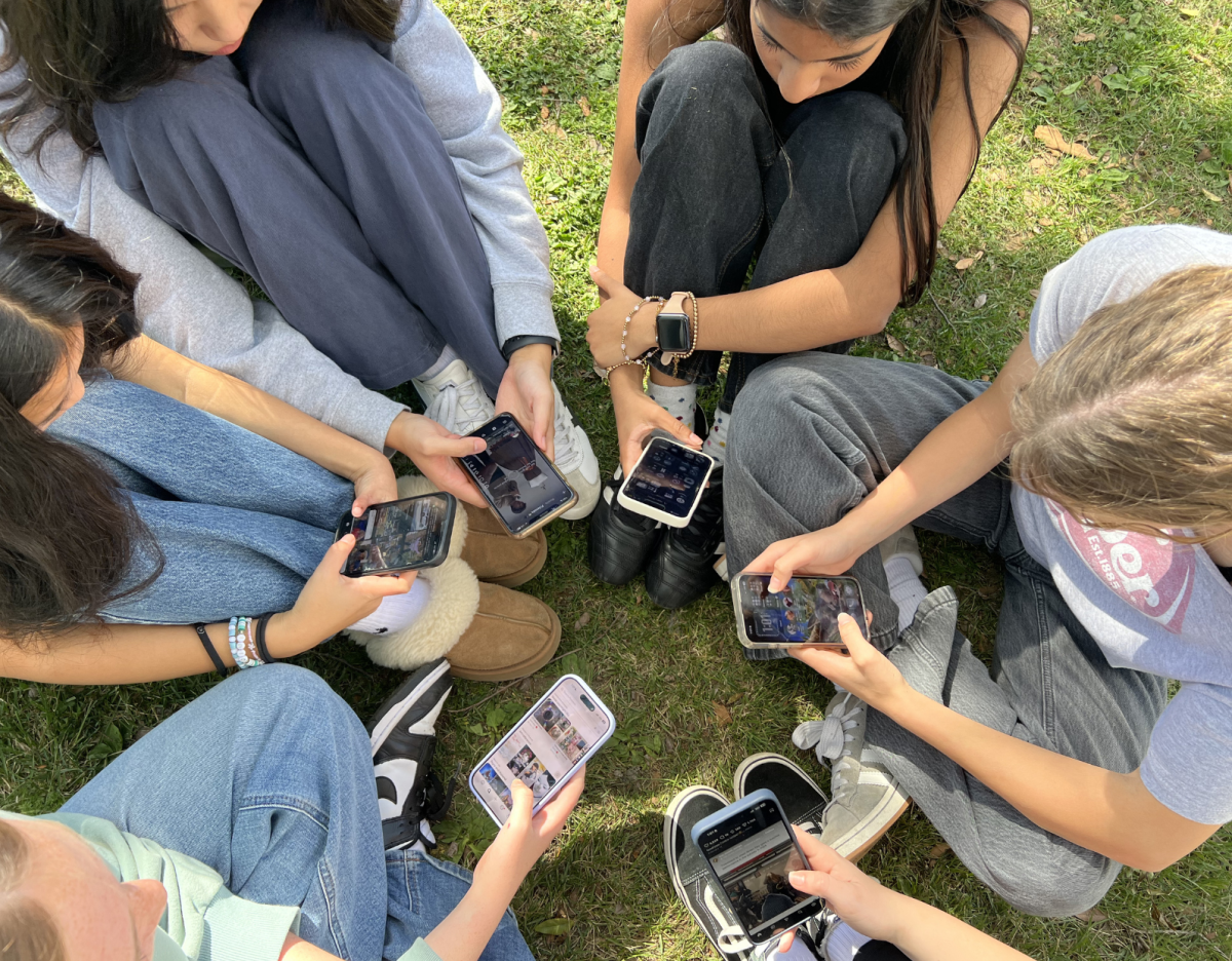 A group of students sitting in a circle, staring at their phones.