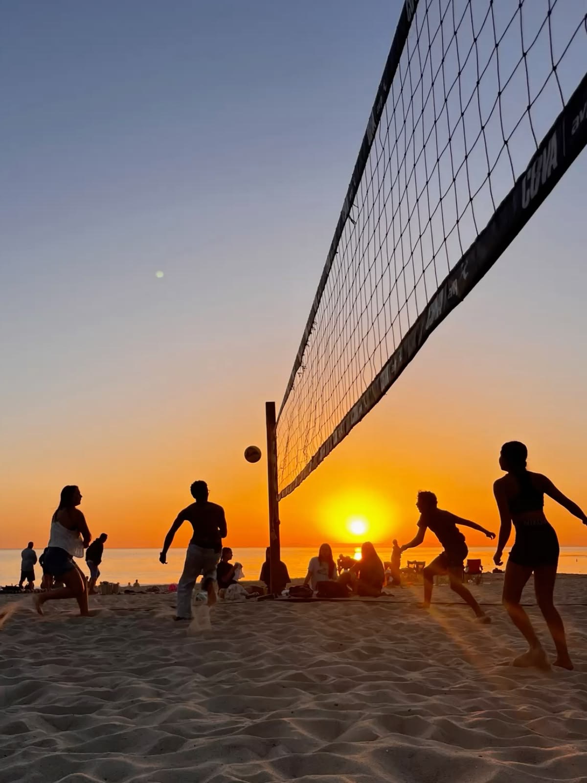 Group of friends playing beach volleyball on the sand during sunset. 